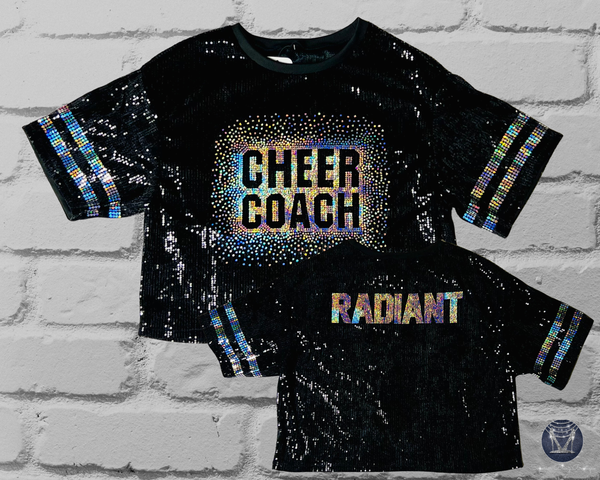 Black sequin jersey with 'CHEER COACH' on front and 'RADIANT' text on back in holographic silver spangle bling on a brick wall background