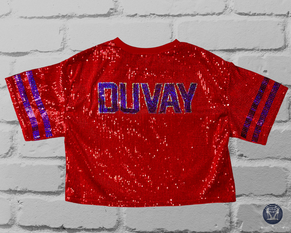A red sequined short-sleeve jersey top shown back on a light gray brick background. The back reads "DUVAY" in blue and silver block letters with blue sleeve stripes.