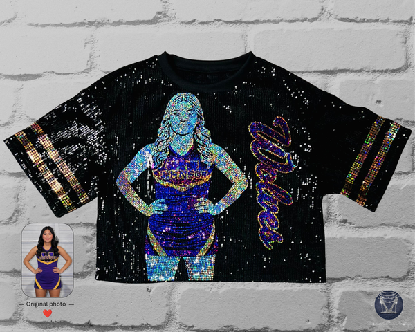 Black sequin jersey with front view of a silver, purple and gold holographic bling portrait of a cheerleader with custom text in cursive. All displayed on a white brick wall. 