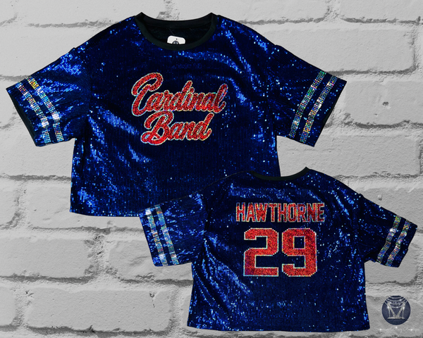 A blue sequined short-sleeve jersey top shown from both front and back on a light gray brick background. The front reads "Cardinal Band" in red and silver script, and the back reads "HAWTHORNE 29" in red and silver block letters with silver sleeve stripes.