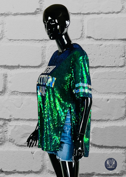 Green sequin top with a side slit, displayed on a mannequin. The top has silver holographic spangle bling stripe design on the sleeves and a lettered design on the front. The mannequin is wearing blue denim shorts.