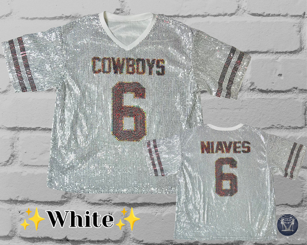 A white sequined football-style jersey shown from the front and back against a white brick wall. The front reads "COWBOYS" and the number 6, with striped sleeve accents. The back shows a custom mane and number six.