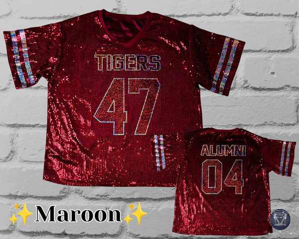 Two maroon sequined football jerseys displayed against a white brick wall background, with the larger front view on the left and a smaller back view on the right. The front jersey reads 'TIGERS' and '47', while the back jersey reads 'ALUMNI' and '04'.