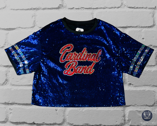 Front view of a blue sequined short-sleeve jersey top on a light gray brick background. The front reads "Cardinal Band" in red and silver script with silver sleeve stripes.