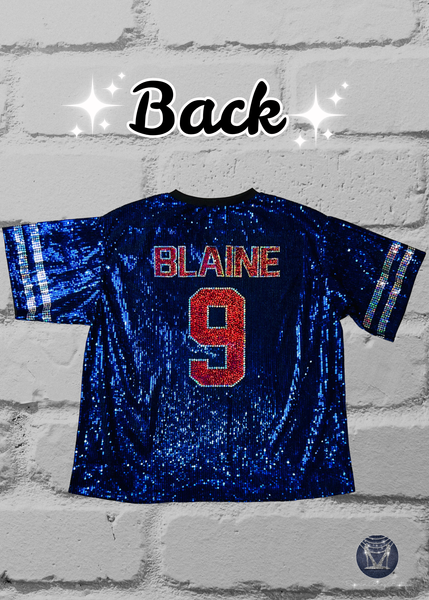 A blue sequined football jersey back view shown on a white brick background. The front features a red and silver bling 'FOOTBALL MOM' graphic with silver sleeve stripes.