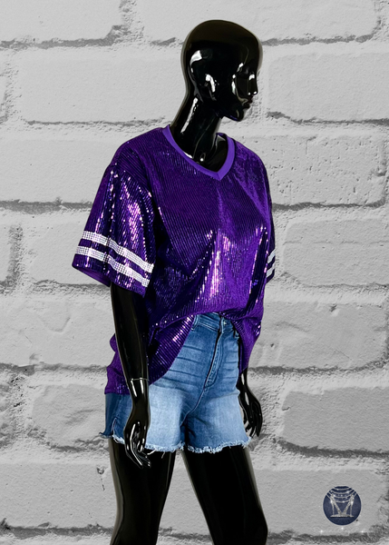 Purple custom football-style sequin jersey shown from the side view with  striped bling white sleeve accents, displayed on a black mannequin against a white brick wall.