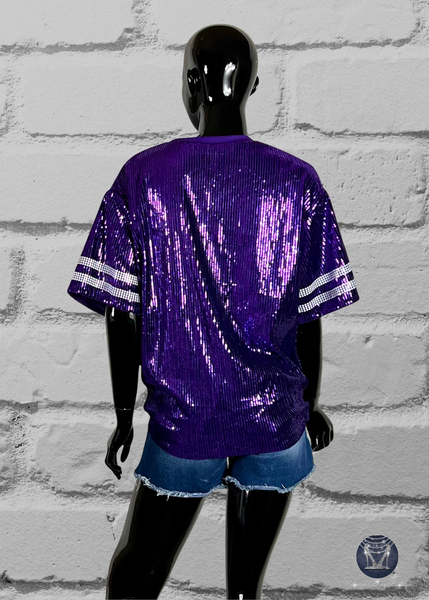 Purple custom football-style sequin jersey shown from the front view with  striped bling white sleeve accents, displayed on a black mannequin against a white brick wall.