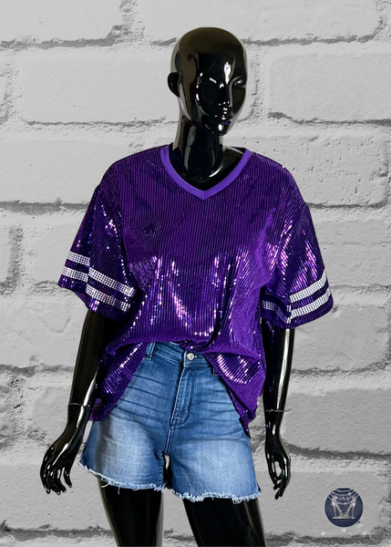 Purple custom football-style sequin jersey shown from the front view with  striped bling white sleeve accents, displayed on a black mannequin against a white brick wall.