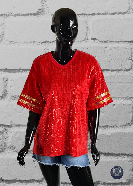 Red custom football-style sequin jersey shown from the front view with  striped bling gold sleeve accents, displayed on a black mannequin against a white brick wall.