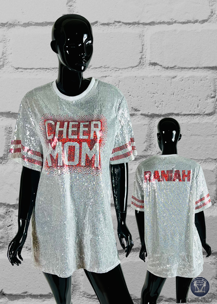 Mannequins wearing sequin 'CHEER MOM' and 'DANIAH' shirts against a white brick wall.