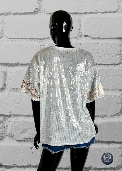 White custom football-style sequin jersey shown from the back view with  striped bling gold sleeve accents, displayed on a black mannequin against a white brick wall.